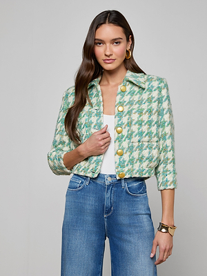 A woman with long brown hair models the Jia Houndstooth Tweed Jacket in jade green over a white top and blue high-waisted jeans, styled with gold hoop earrings and a bracelet, against a plain light background.