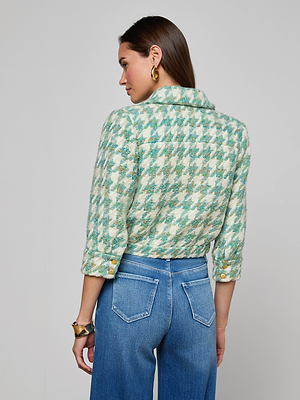 A woman with long brown hair and gold hoop earrings wears the Jia Houndstooth Tweed Jacket in jade green with rolled sleeves and gold buttons, paired with high-waisted blue jeans, facing away.