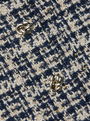 Close-up of the Jia Tweed Jacket by L'AGENCE, featuring textured navy blue, white, and gold woven fabric with two gold knot-shaped buttons.