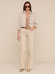 A woman wearing sunglasses, the Jia Cropped Tweed Jacket with three-quarter sleeves, a tan top, wide-leg beige pants, and heels stands against a plain white background with her hands in her pockets.