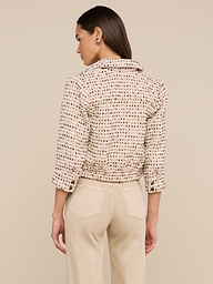 A woman with straight hair tucked behind her ear and round gold earrings stands with her back facing the camera. She is wearing an ivory Jia Cropped Tweed Jacket featuring three-quarter sleeves, paired with beige pants. The background is plain and light.
