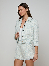 A woman wearing the Jia Fringed Tweed Jacket in light blue with large buttons and matching high-waisted shorts, standing against a plain white background.