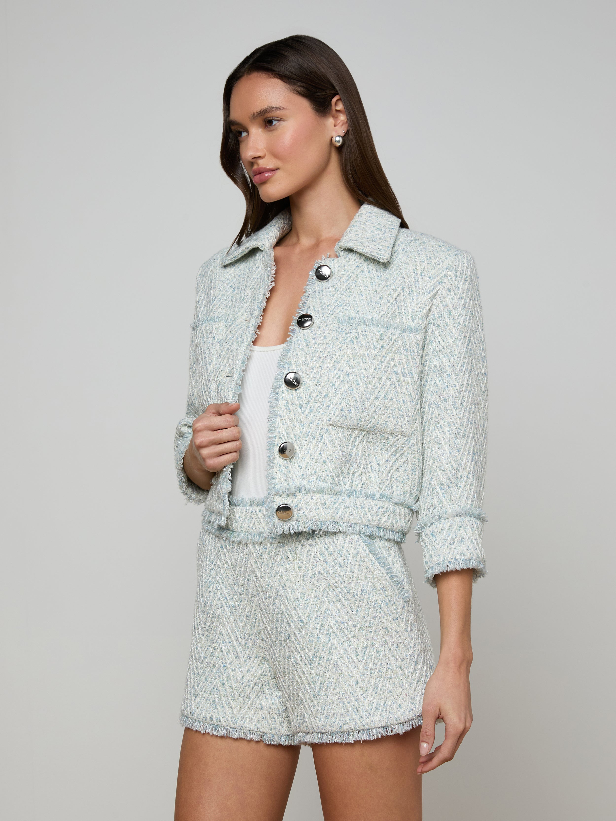A woman wearing the Jia Fringed Tweed Jacket in light blue with large buttons and matching high-waisted shorts, standing against a plain white background.