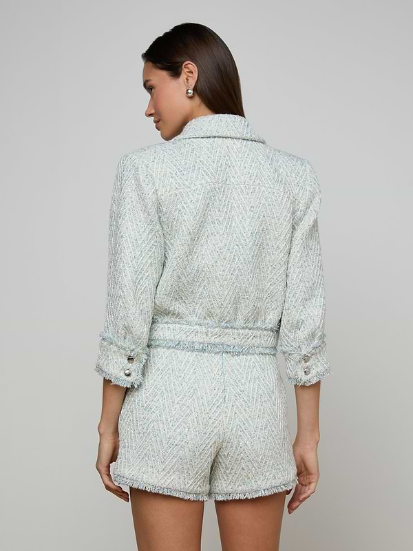 A woman with long brown hair, facing away from the camera against a plain, light background, is wearing the Jia Fringed Tweed Jacket with matching shorts.