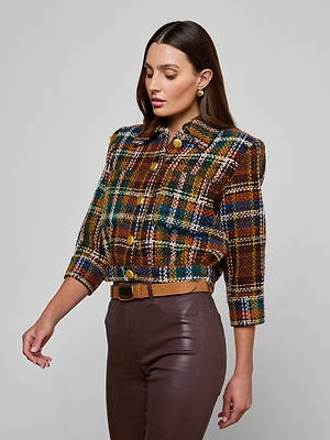 A woman with long brown hair wears the Jia Cropped Tweed Jacket, featuring a multicolored plaid bouclé tweed fabric and gold buttons, styled with brown high-waisted pants, a tan belt, and gold earrings against a light gray background.