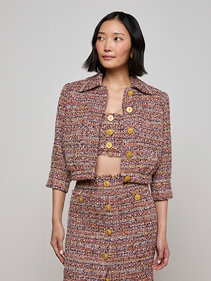 A woman wears the L'AGENCE Sale Jia Tweed Jacket, featuring three-quarter sleeves and lion head buttons, paired with a matching skirt and cropped top, standing against a plain light background.