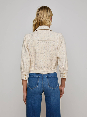 A person with long blonde hair wears the Jia Sequined Tweed Jacket by L'AGENCE Sale, featuring ecru tweed and three-quarter sleeves, paired with blue jeans, standing with their back to a plain light gray background.