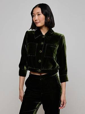 A woman with medium-length black hair wears the L'AGENCE Jia Velvet Jacket in olive green, styled with matching pants, standing against a plain light gray background.