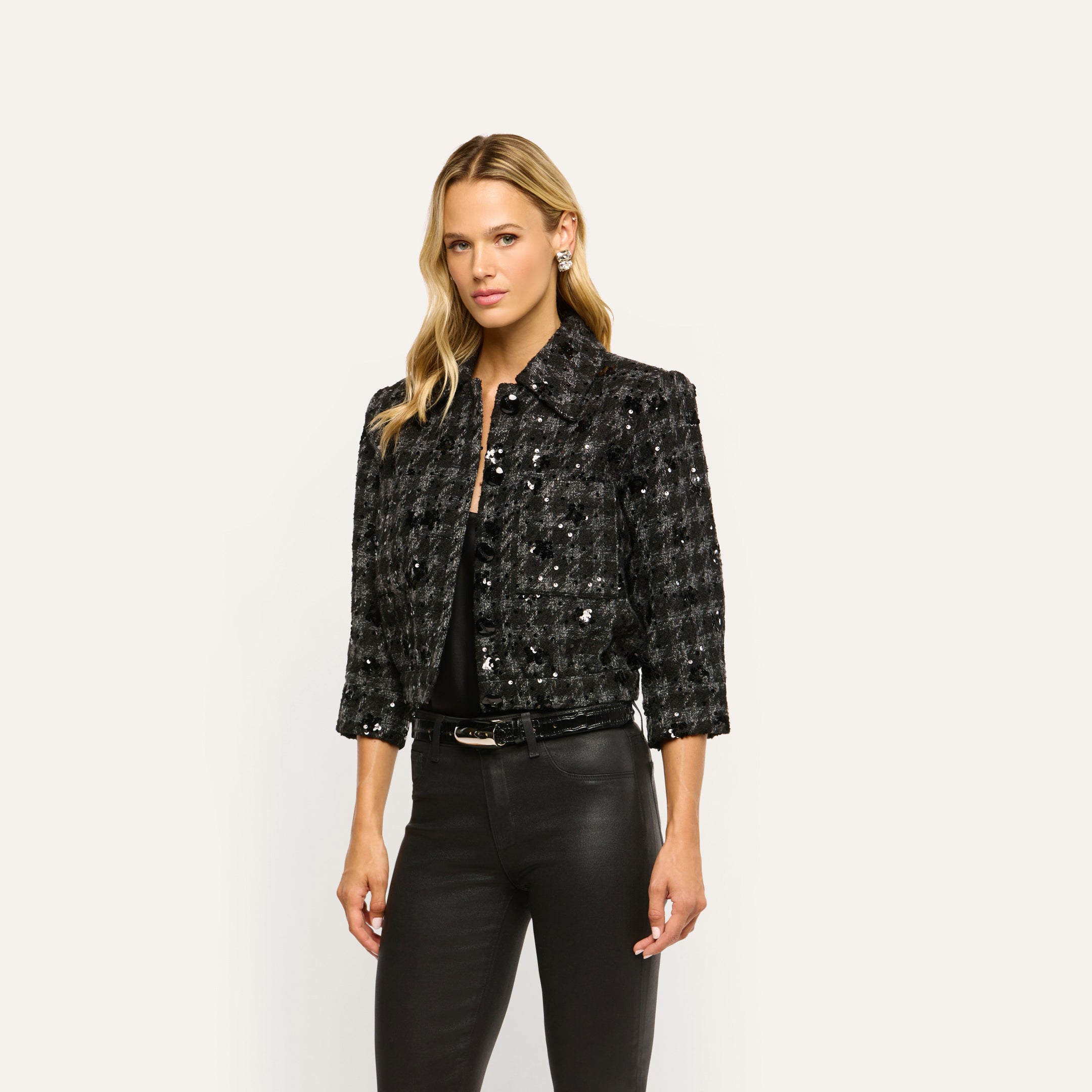 A woman wears a black, cropped Jia Sequined Tweed Jacket paired with black pants.