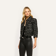 A woman wears a black, cropped Jia Sequined Tweed Jacket over a black top and pants.