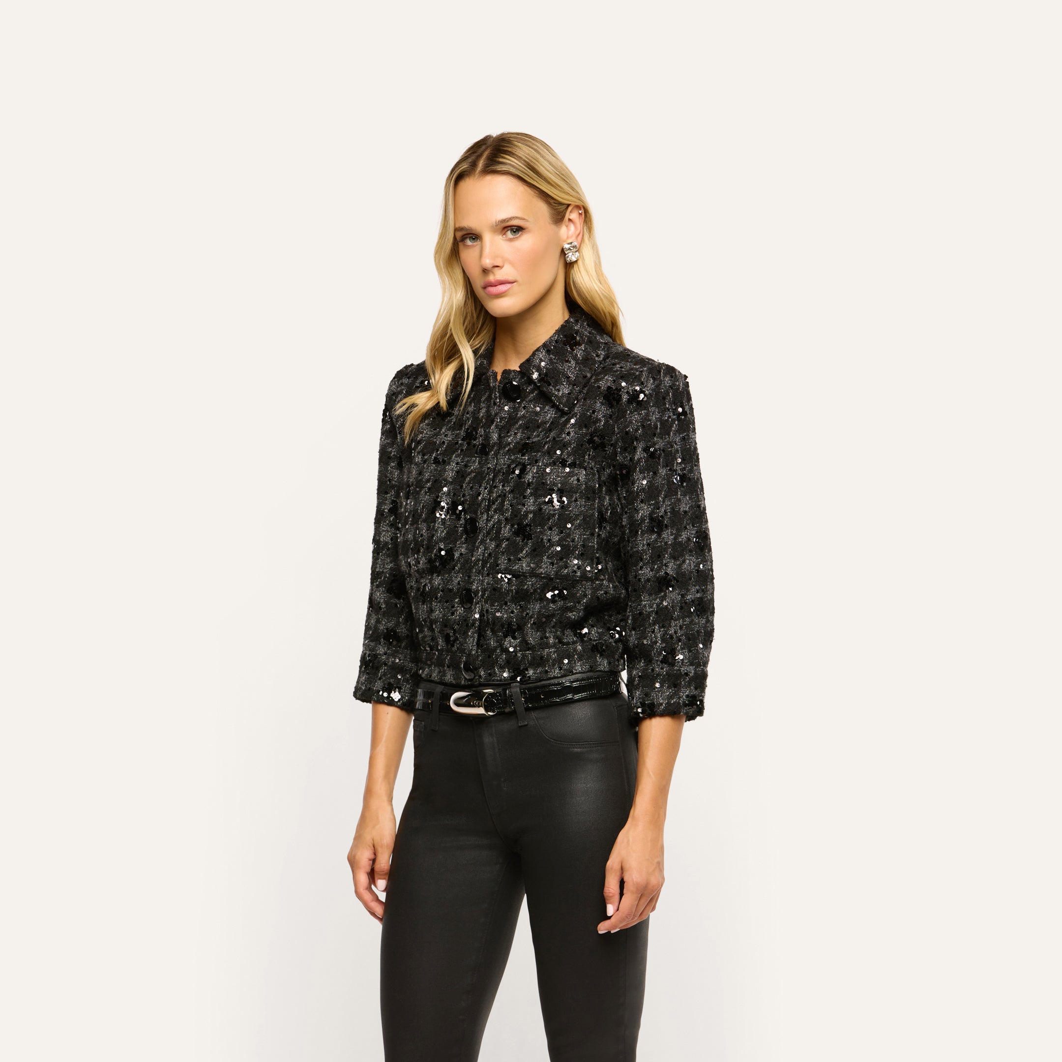 A model wearing a black Jia Sequined Tweed Jacket with three-quarter sleeves and belted black trousers.