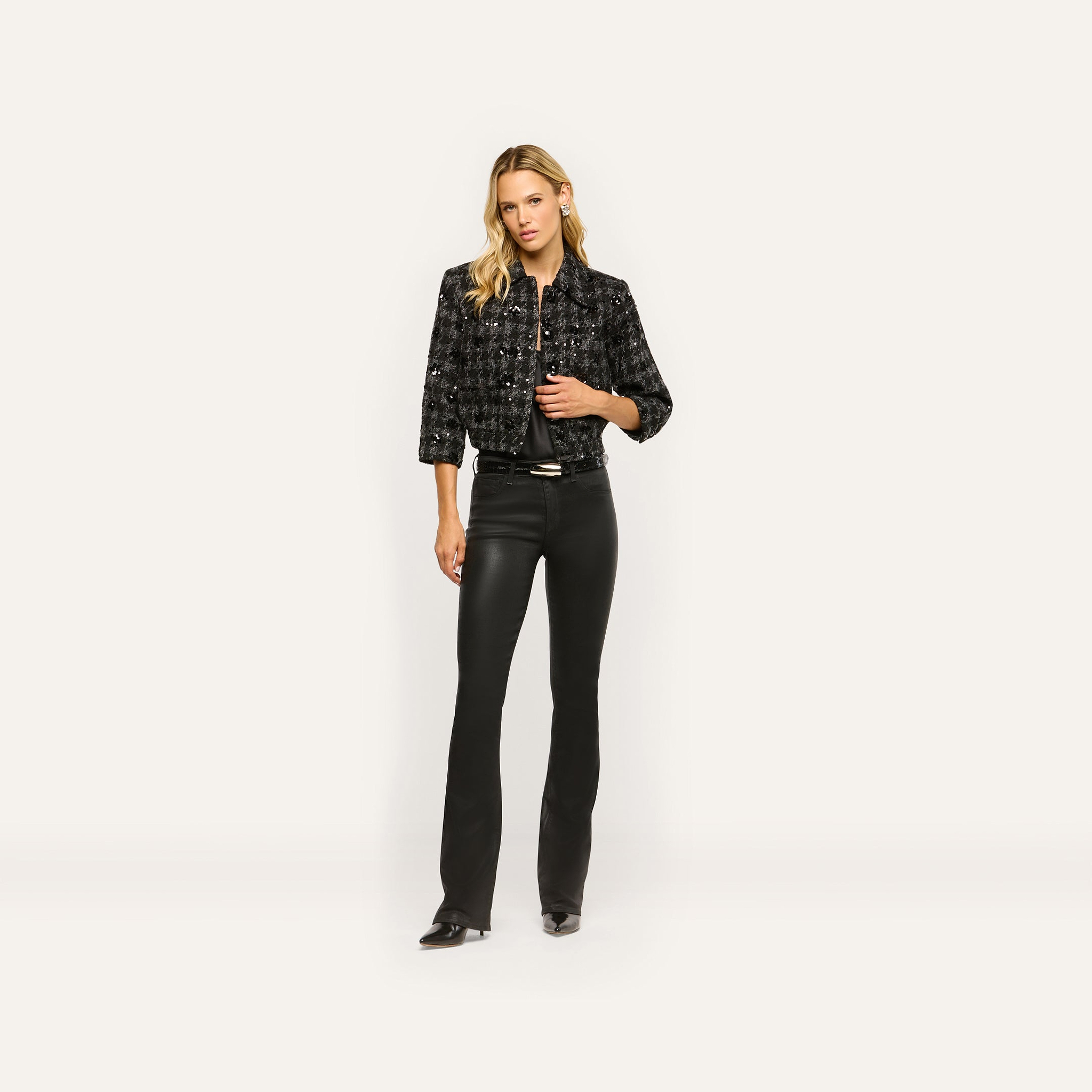 A woman wearing a black Jia Sequined Tweed Jacket over a black top and black flared trousers.