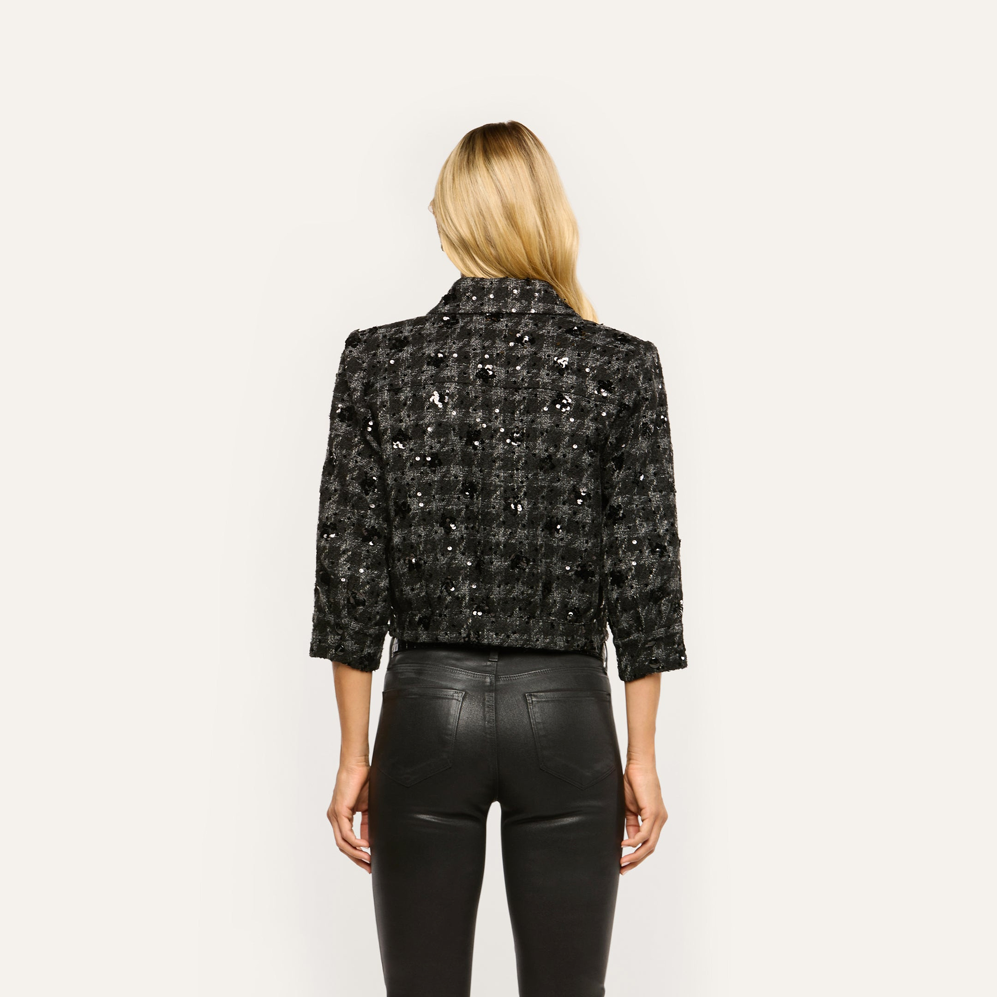 Back view of a person wearing a cropped, black-and-grey sequin Jia Sequined Tweed Jacket with three-quarter length sleeves, paired with black pants.