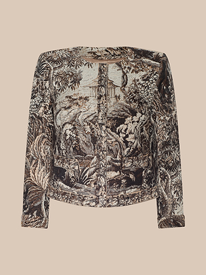 The Lian Tapestry Jacket is a long-sleeve, collarless jacket in Italian jacquard, showcasing a detailed nature scene with trees and foliage in earthy brown, beige, and green on a beige background.