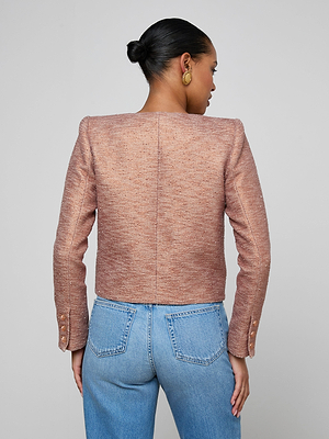 A woman with her hair in a bun models the Zell Tweed Jacket—textured, collarless, and paired with high-waisted light blue jeans—facing away from the camera against a plain light background.