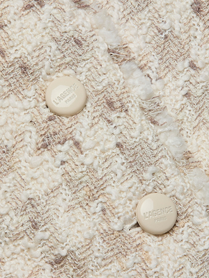 Close-up of the Zell Houndstooth Tweed Jacket, featuring cream and beige textured wool-blend fabric and two round beige buttons embossed with 