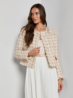 A woman with long brown hair wears the Zell Houndstooth Tweed Jacket over a light blouse and high-waisted white pants, creating a feminine silhouette against a plain light gray background as she looks to her left.