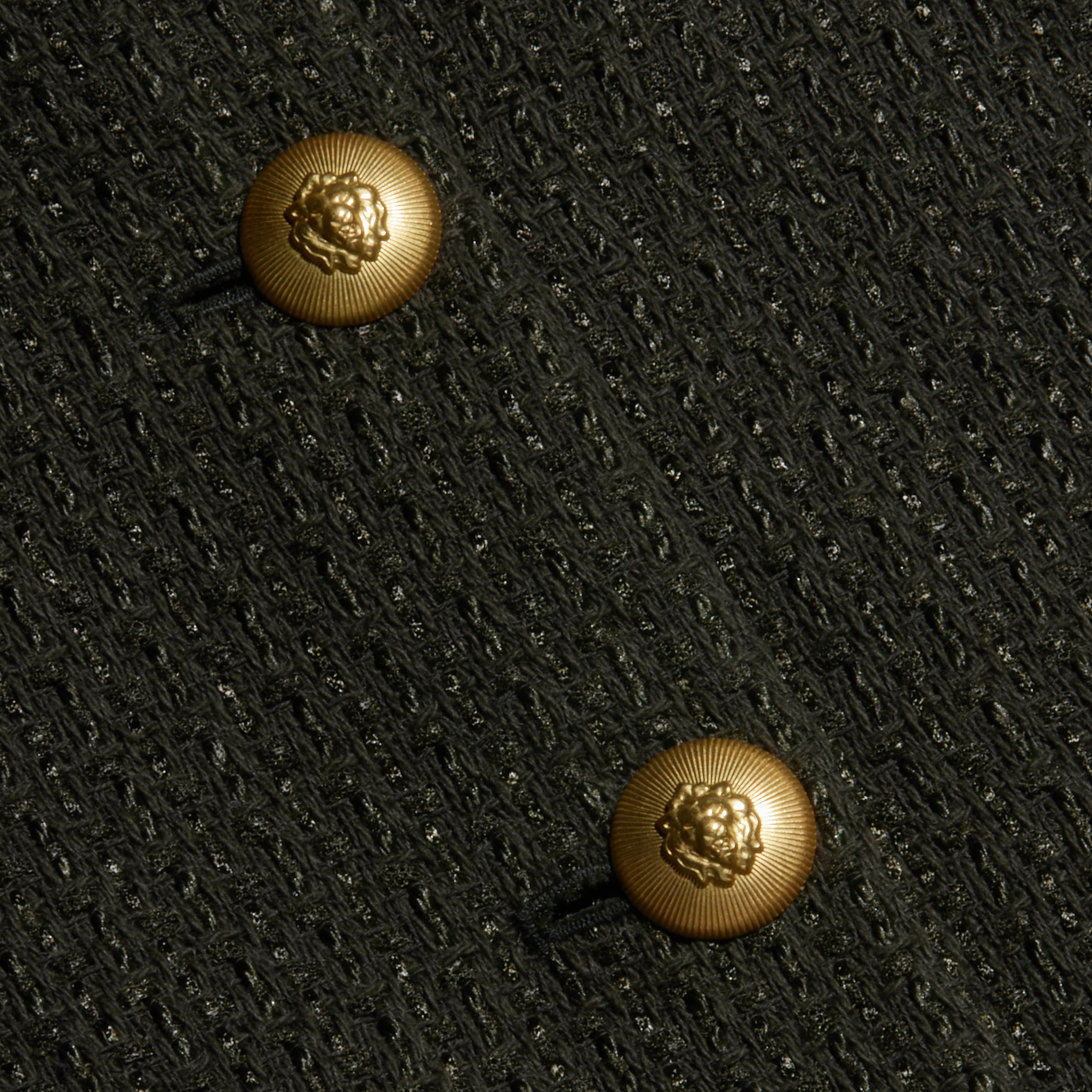 Close-up of two gold lion-embossed buttons on the textured black Zell Tweed Jacket.