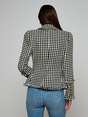 A woman with long brown hair, seen from behind, wears the Kaisley Tweed Blazer in black and ivory with gold sleeve buttons and light blue jeans. The blazer stands out against the plain, light-colored background.