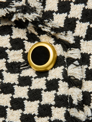 Close-up of the Kaisley Tweed Blazer, featuring a black and white houndstooth pattern and a round gold-and-black button.