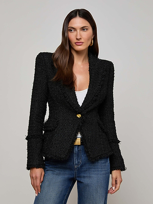 A woman with long brown hair models the L'AGENCE Kaisley Frayed Trim Blazer, featuring a single gold button, over a white top and blue jeans against a plain light gray background.