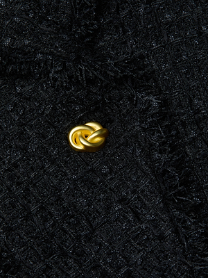 A close-up of the L’AGENCE Kaisley Frayed Trim Blazer, showcasing its textured black tweed and single gold knot-shaped button.