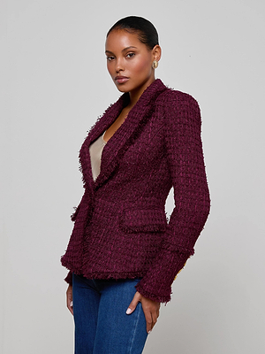 A woman with slicked-back hair models the L'AGENCE Kaisley Tweed Blazer in maroon over a beige top and blue jeans, posing against a plain light gray background.