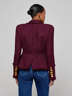 A woman with her hair in a low bun is seen from behind wearing the L'AGENCE Kaisley Tweed Blazer in maroon with gold sleeve buttons and blue jeans, standing against a plain light gray background.