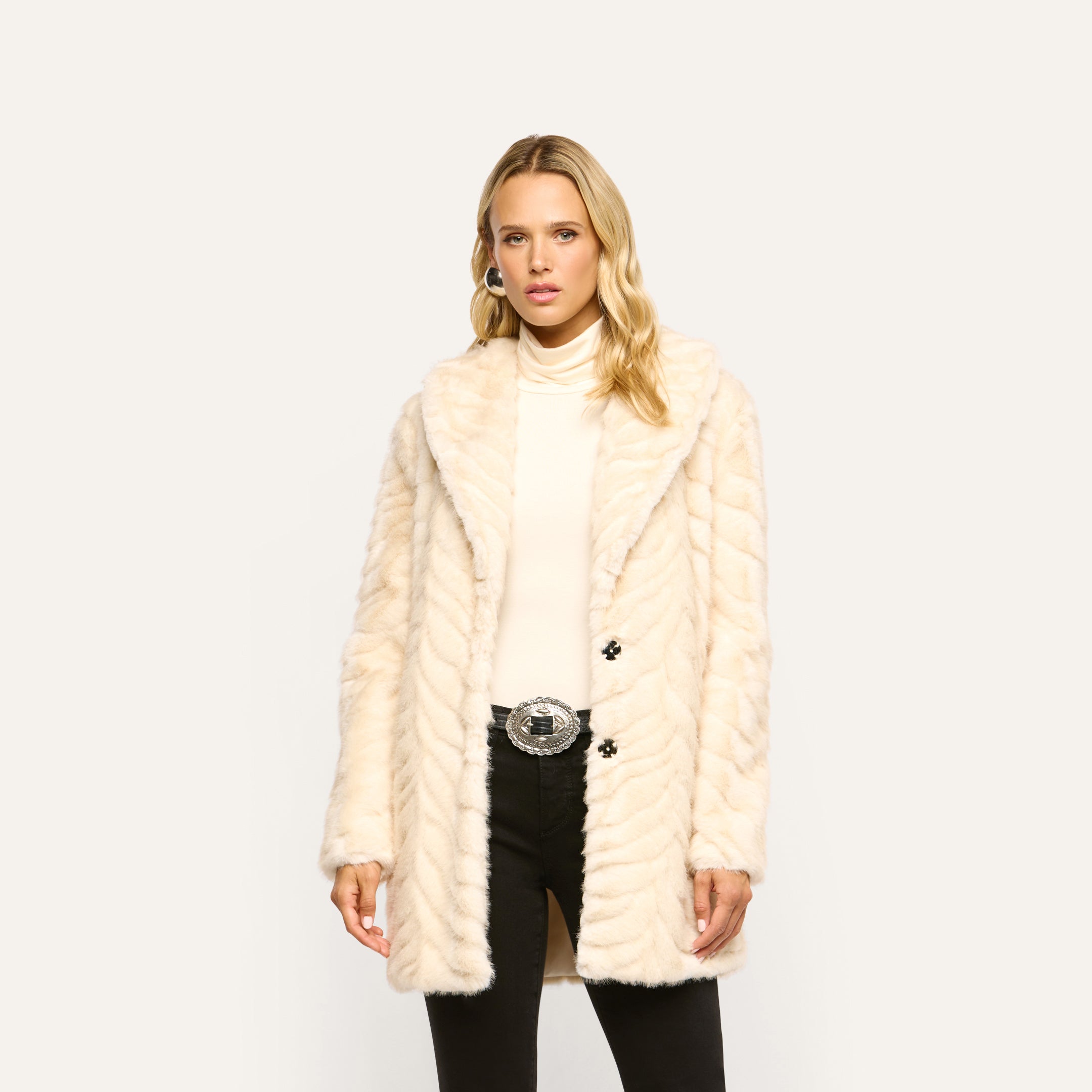 Woman wearing a 70s-inspired chevron pattern Toira Faux Fur Coat over a turtleneck and black pants.