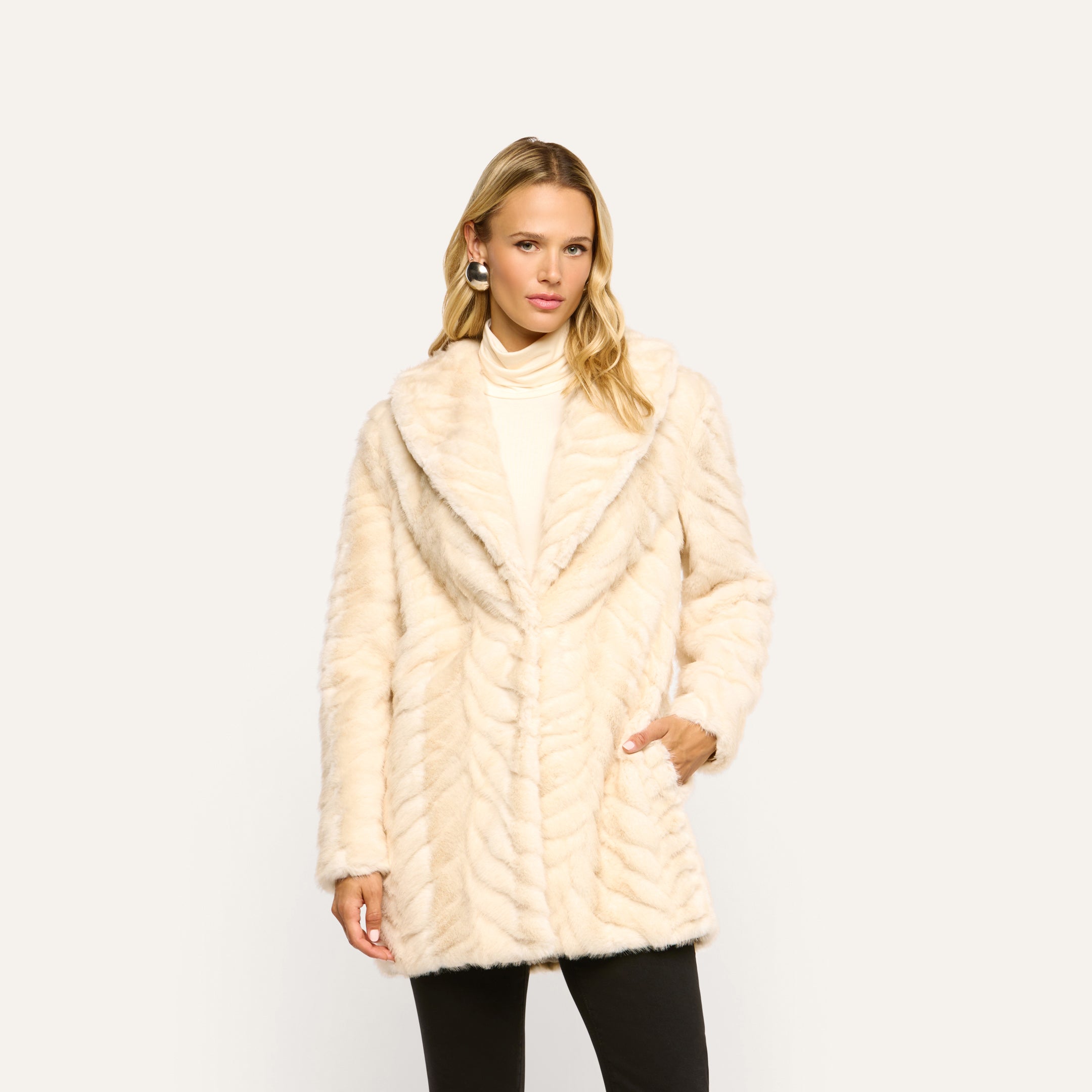 The Toira Faux Fur Coat is a cream-colored, 70s-inspired design featuring a wide lapel and a distinctive chevron-patterned texture.