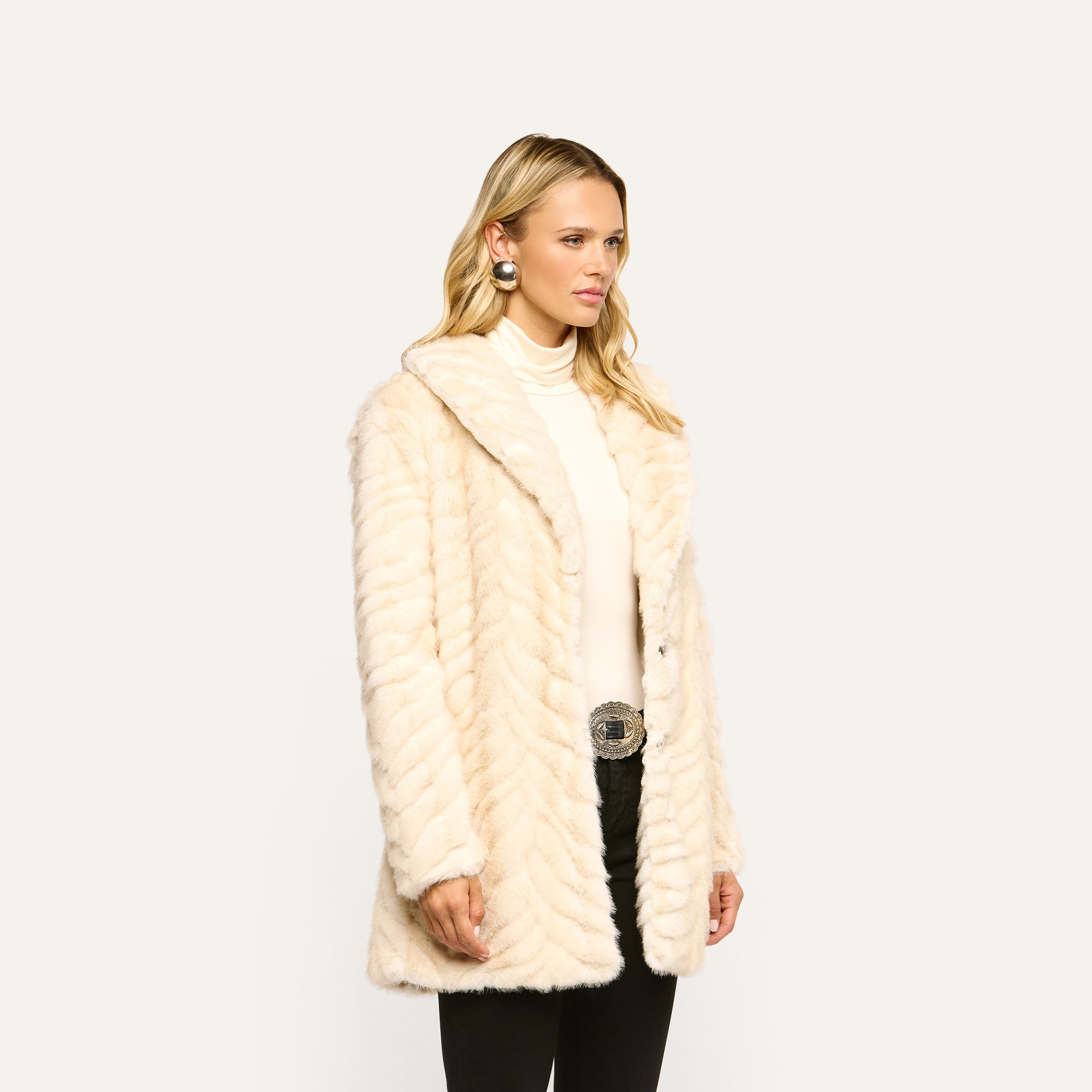 A woman wearing a Toira Faux Fur Coat in a 70s-inspired textured chevron pattern over a turtleneck and black pants.