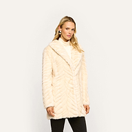 A woman wears a Toira Faux Fur Coat in a 70s-inspired cream chevron pattern over a turtleneck sweater.