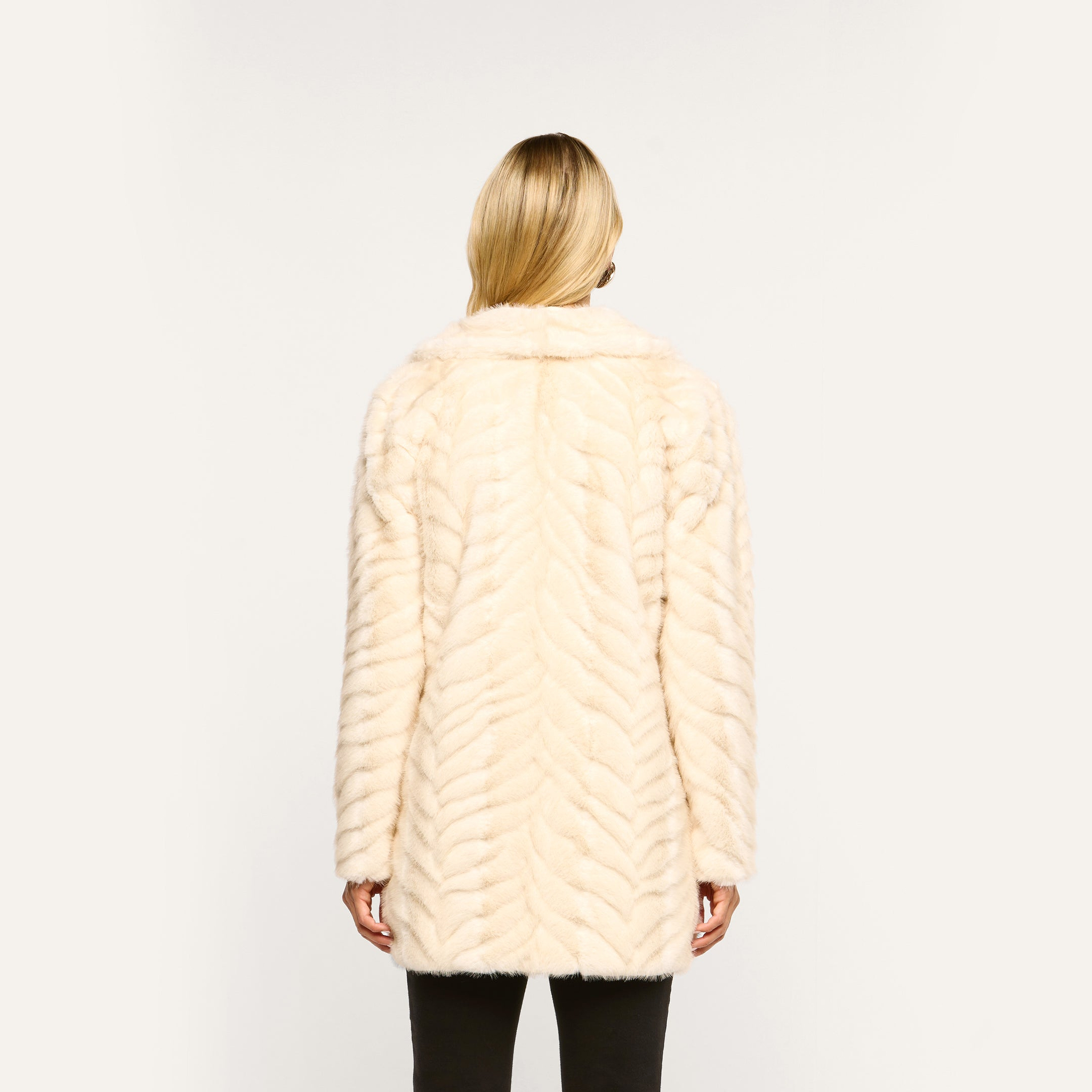 Back view of a person wearing a cream-colored Toira Faux Fur Coat in a 70s-inspired chevron pattern.