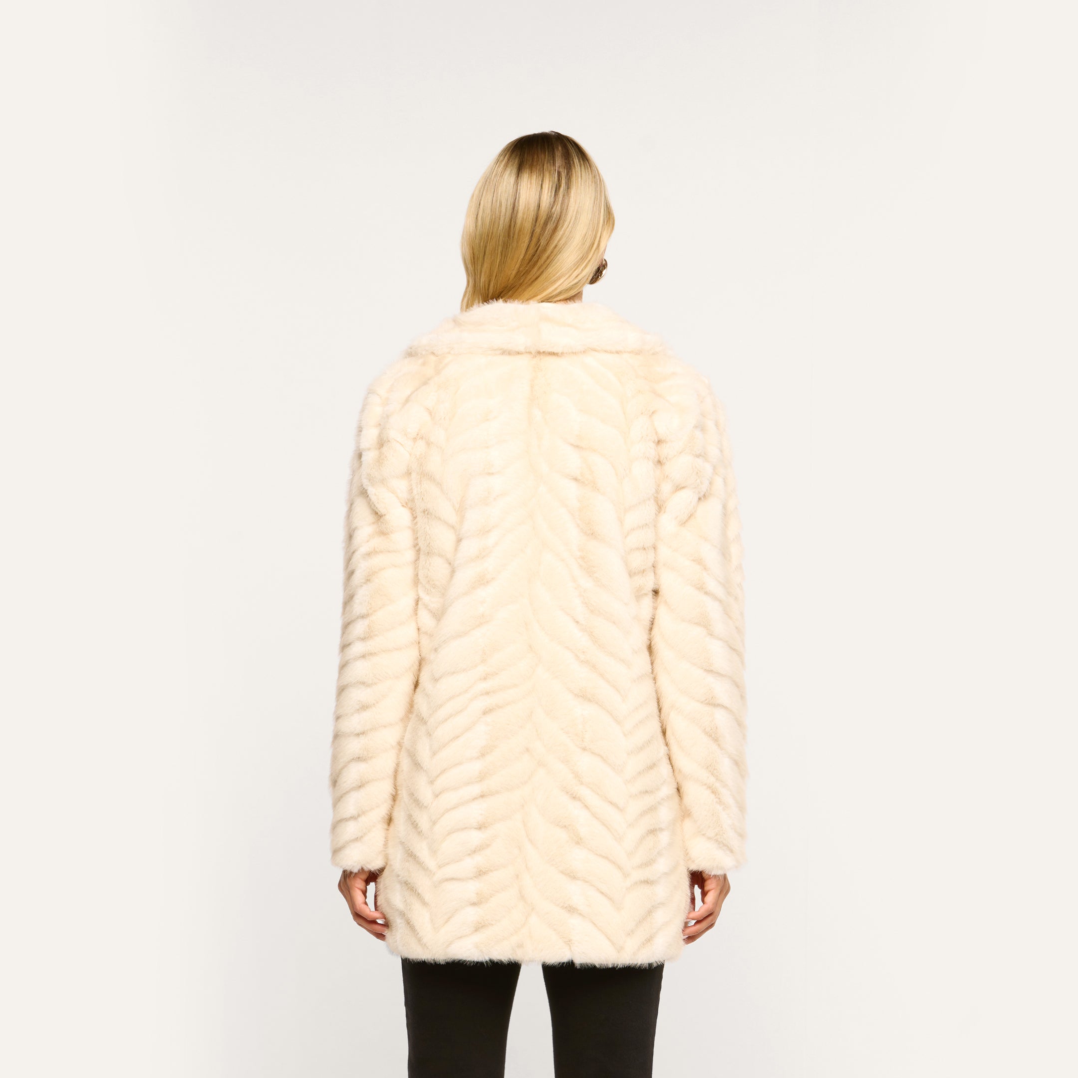Back view of a person wearing a cream-colored Toira Faux Fur Coat in a 70s-inspired chevron pattern.