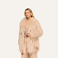 Wearing the Toira Faux Fur Coat in a fluffy beige finish over a sparkly outfit, the person stands against a plain, light background, channeling a vintage-inspired 70s rockstar vibe.