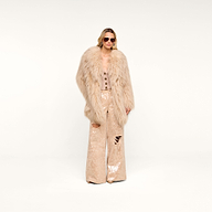 A woman wearing sunglasses, the Toira Faux Fur Coat—a vintage-inspired beige faux fur coat—a beige buttoned top, and beige sequin wide-leg pants with rips stands against a plain white background.