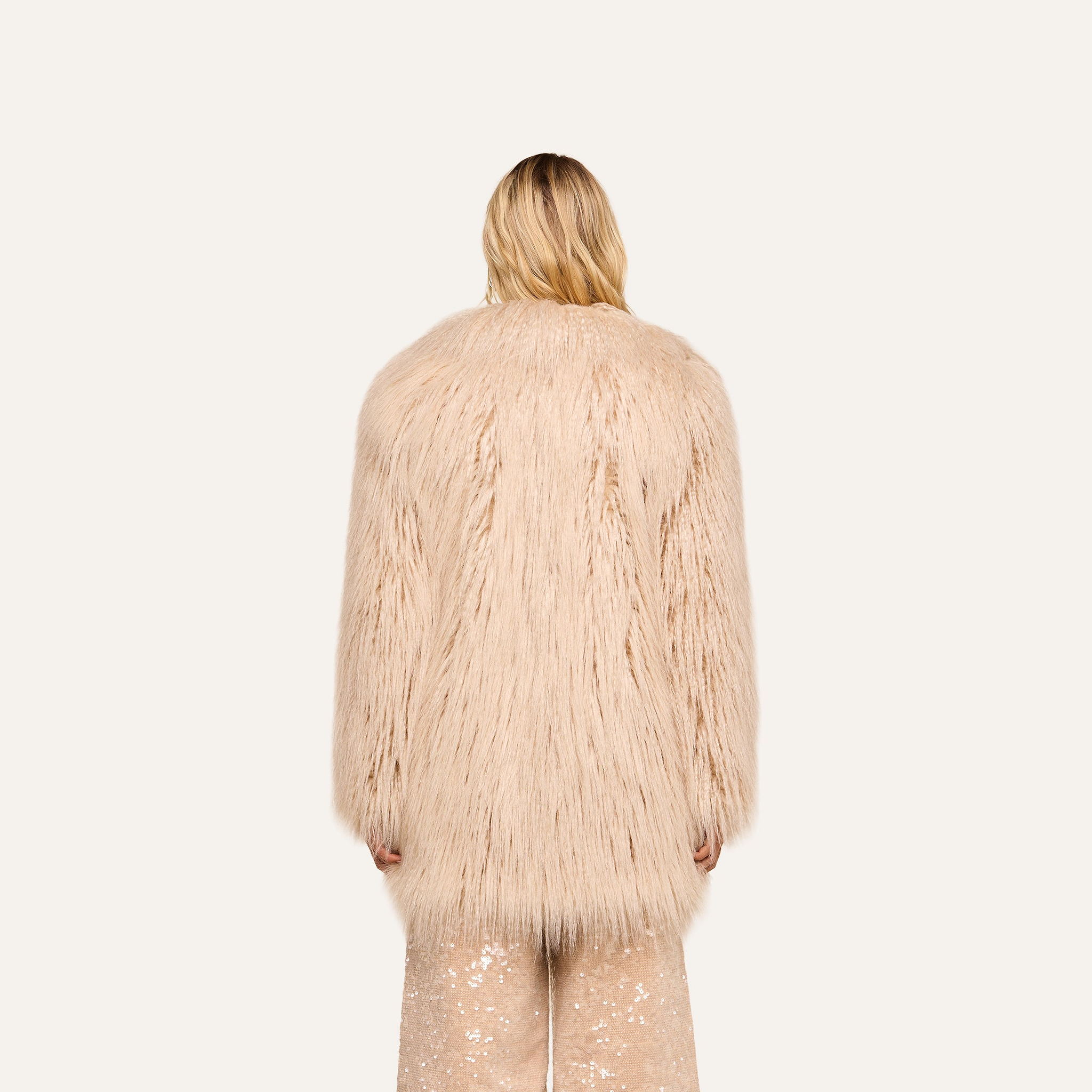 A person with blonde hair, seen from behind, wears the Toira Faux Fur Coat and sparkly beige pants against a plain light background, channeling a vintage-inspired 70s rockstar vibe.