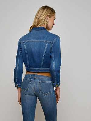 A woman with blonde hair models the L'AGENCE Koda Cropped Jean Jacket, seen from the back against a plain light gray background.