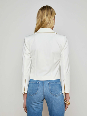 A woman with long blonde hair is seen from the back wearing the L'AGENCE Calianna Shirt Jacket—fitted and white with gold zipper sleeve accents—paired with high-waisted blue jeans and gold bangles on her left wrist.
