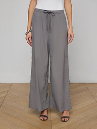 A person wearing loose, gray Valkyrie Snap Pants with a relaxed fit, paired with black heeled sandals and a white top. The image is cropped at the shoulders.