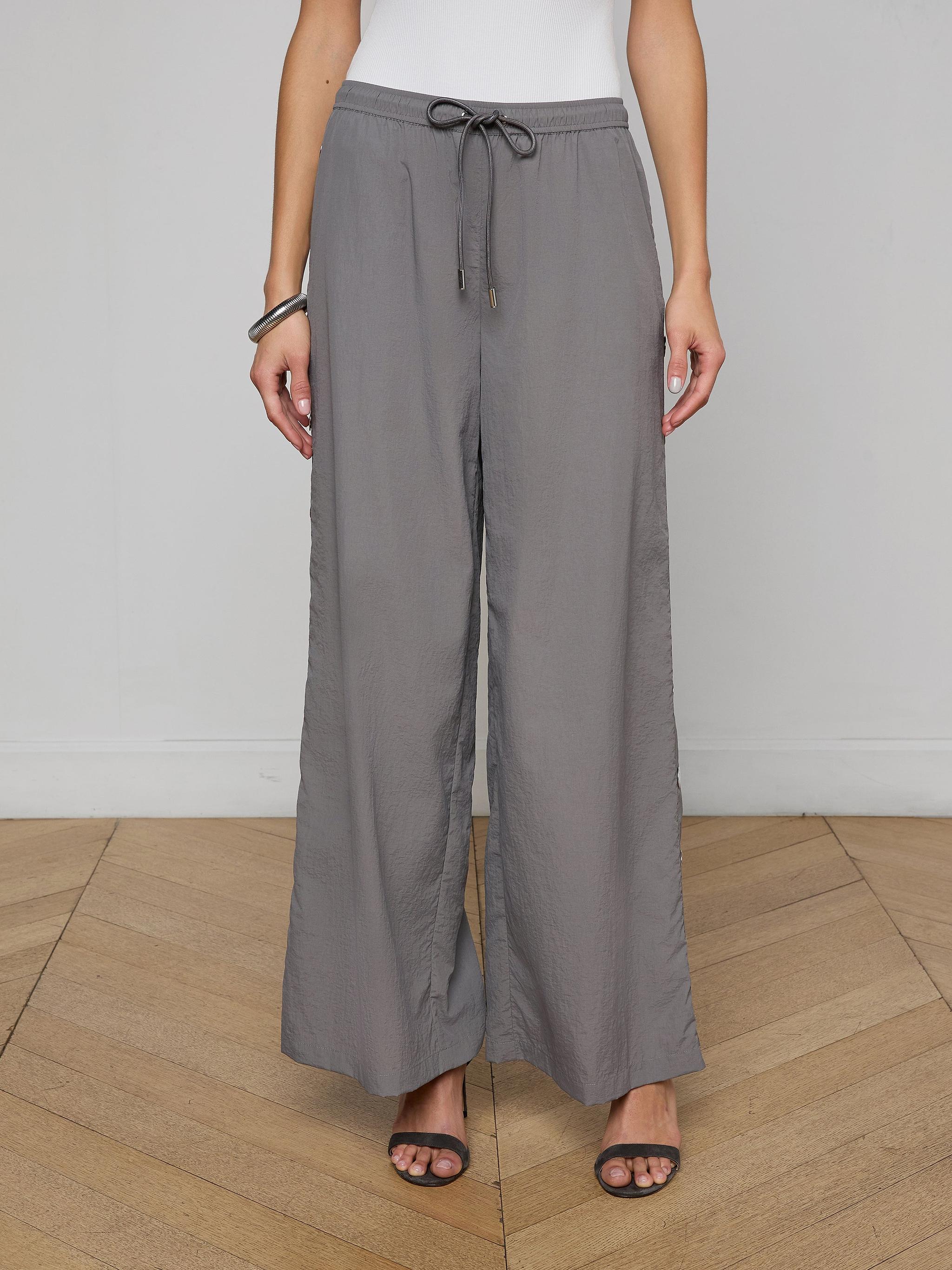 A person wearing loose, gray Valkyrie Snap Pants with a relaxed fit, paired with black heeled sandals and a white top. The image is cropped at the shoulders.