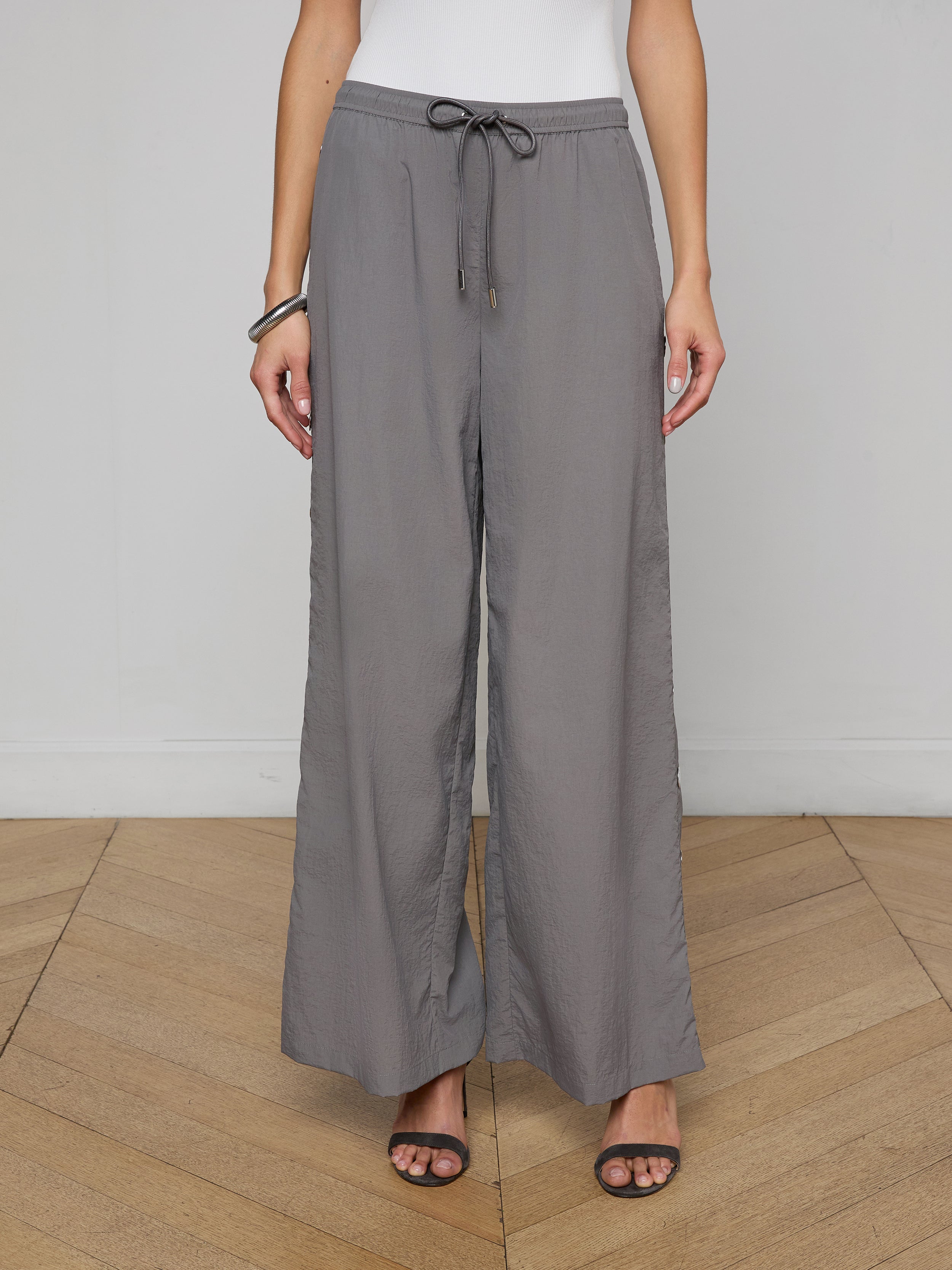 A person wearing loose, gray Valkyrie Snap Pants with a relaxed fit, paired with black heeled sandals and a white top. The image is cropped at the shoulders.