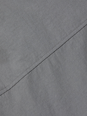 Close-up of the Bronwyn Cropped Windbreaker's light gray, water-repellent fabric, featuring a diagonal seam and visible stitching that highlight the texture of the material.