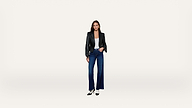A woman stands facing forward, wearing a black jacket, white top, wide-leg blue jeans, and black heels, against a plain white background.