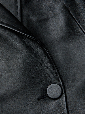 Close-up of the Vashti Fringed Leather Blazer by L’AGENCE, crafted from smooth black Italian lambskin and featuring textured material, a defined lapel fold, and a round black button.