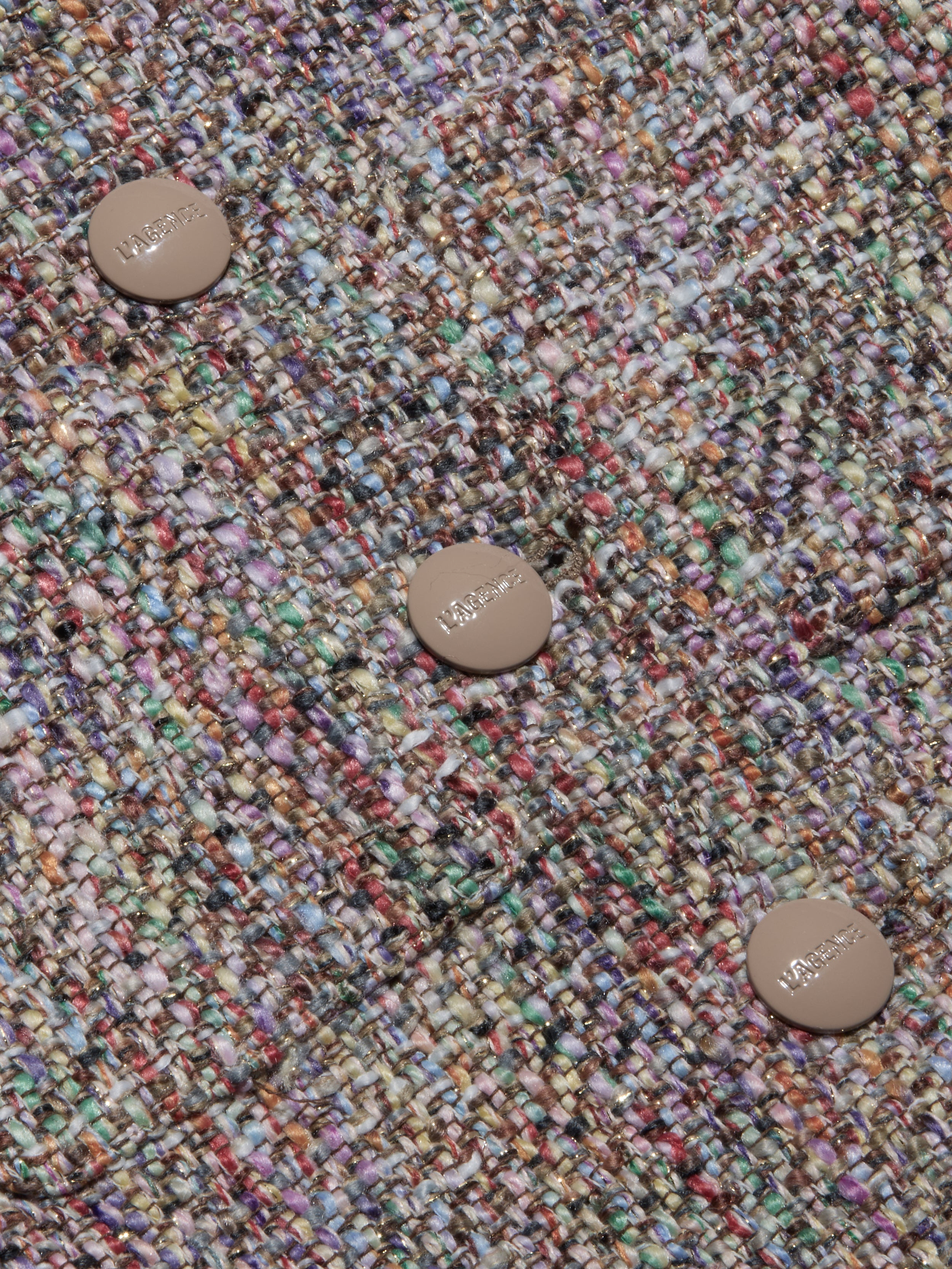 Close-up of the Chita Tweed Jacket’s multi-colored tweed fabric, featuring three beige buttons engraved with ‘MAJE’. The textured threads—shades of purple, green, yellow, and red—create a vibrant woven pattern that highlights the jacket’s distinctive cropped style.