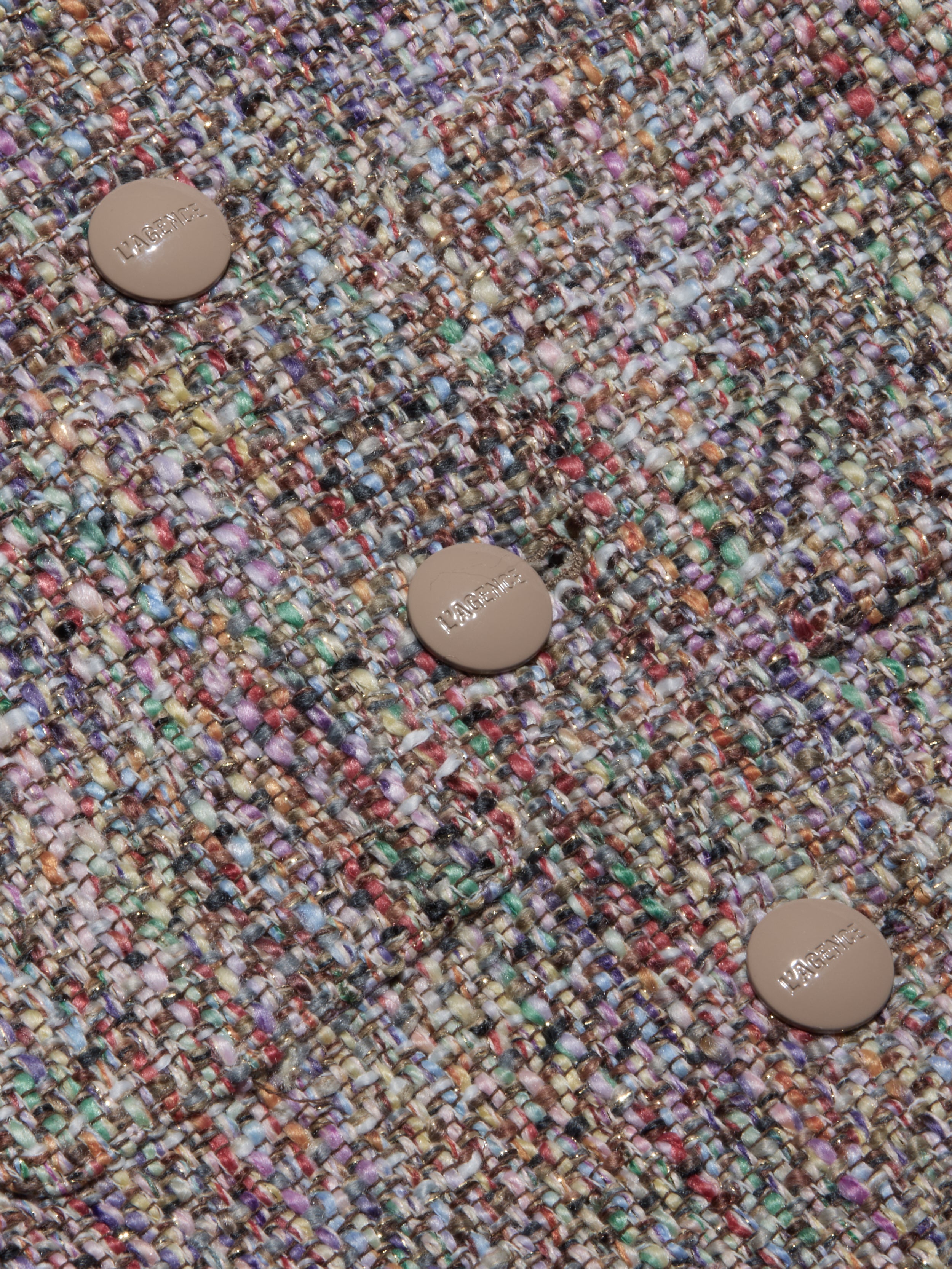 Close-up of the Chita Tweed Jacket’s multi-colored tweed fabric, featuring three beige buttons engraved with ‘MAJE’. The textured threads—shades of purple, green, yellow, and red—create a vibrant woven pattern that highlights the jacket’s distinctive cropped style.