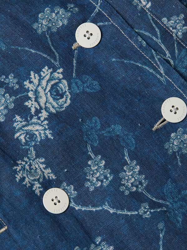 Close-up of the Bradley Linen Trench Coat in blue, featuring white floral patterns and buttons along stitched seams. Detailed roses and branches create a vintage, elegant style—perfect for a lightweight outer layer or linen jacket.