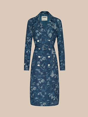 The Bradley Linen Trench Coat, featuring a blue and white floral design, double-breasted buttons, matching belt, and lapel collar, adds classic style as a lightweight outer layer, shown on a plain beige background.