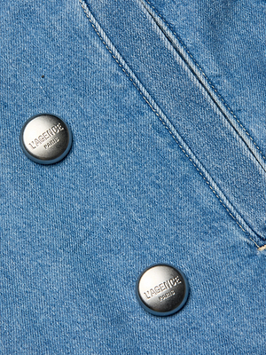 Close-up of medium wash denim fabric from the Bradley Trench Coat, showcasing two metallic LAGENCE PARIS-embossed buttons and detailed stitching.